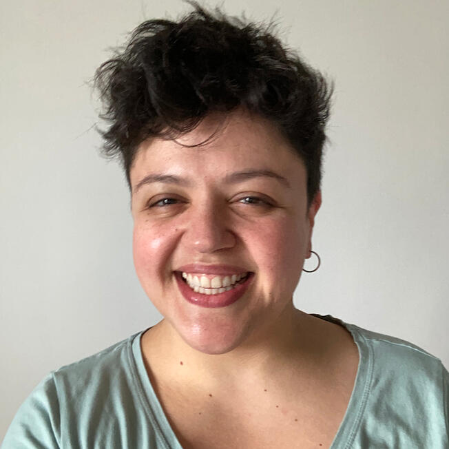 A portrait photo of Clau, who has short dark hair, a light blue top and is smilling.